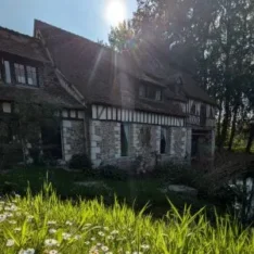 Façade du Moulin d'Andé entourée de verdure et de marguerites au soleil — lieu d'immersion résidentielle pour la formation en aromathérapie énergétique en Normandie