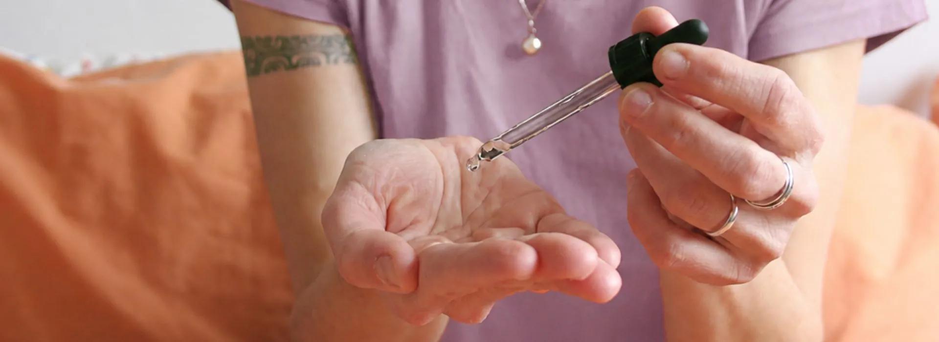 Femme déposant une goutte d'huile essentielle au creux de sa main avec une pipette, geste d'application découvert lors de l'atelier d'aromathérapie énergétique