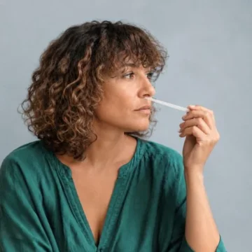 Femme en chemise verte sentant une touche à sentir imprégnée d'huile essentielle, geste d'olfaction pratiqué en atelier d'aromathérapie énergétique